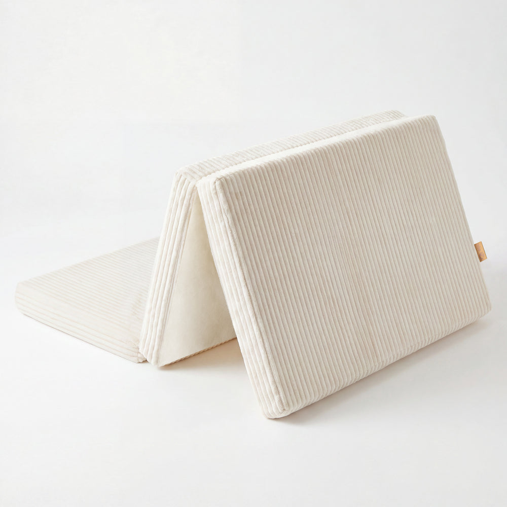 Freisteller der Reisebettmatratze in Beige mit Cord-Bezug, halb aufgeklappt aufgestellt vor weißem Hintergrund.