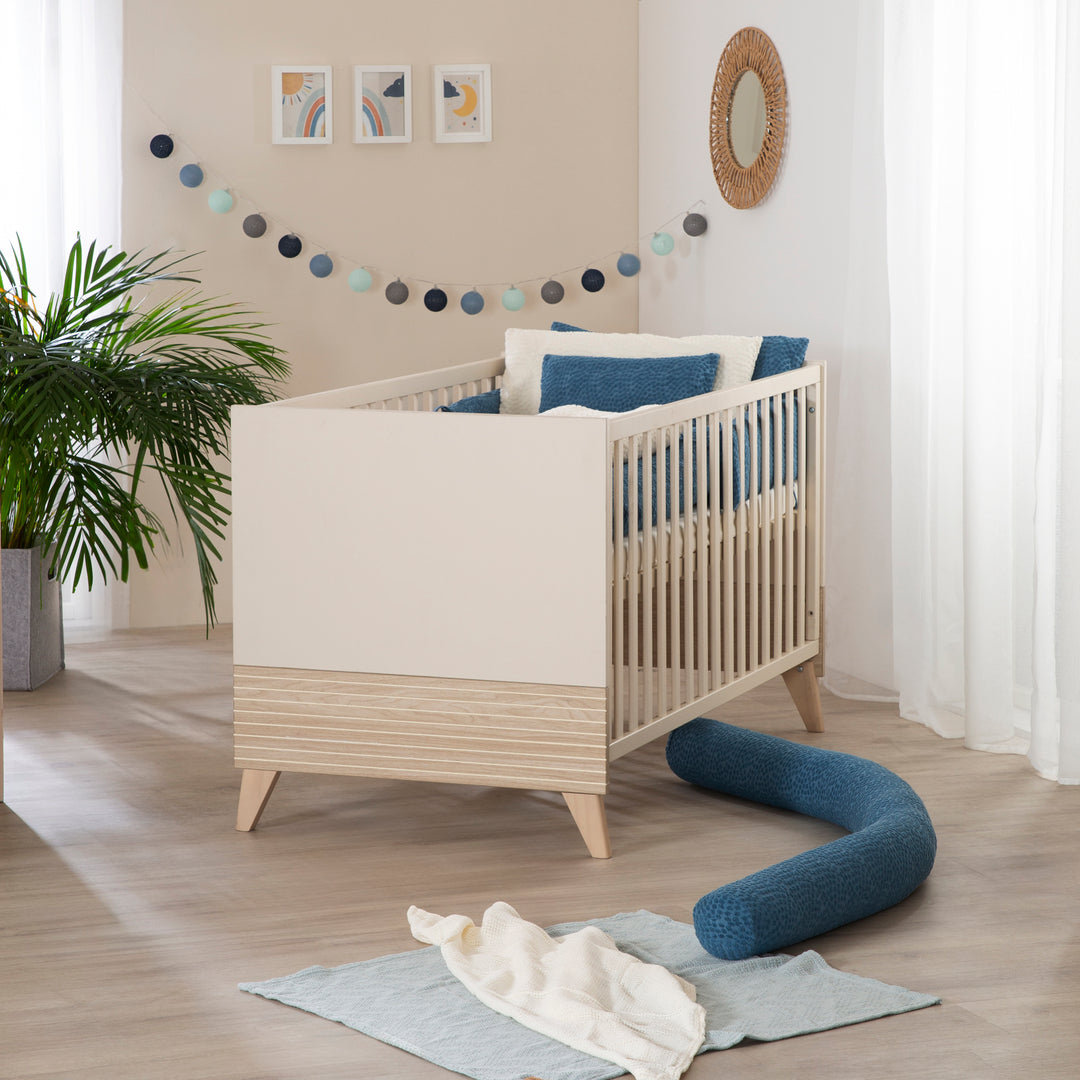 Babybett 'Sidney' im Babyzimmer mit blauer Bettwäsche, Nestchenschlange und Zimmerpflanze
