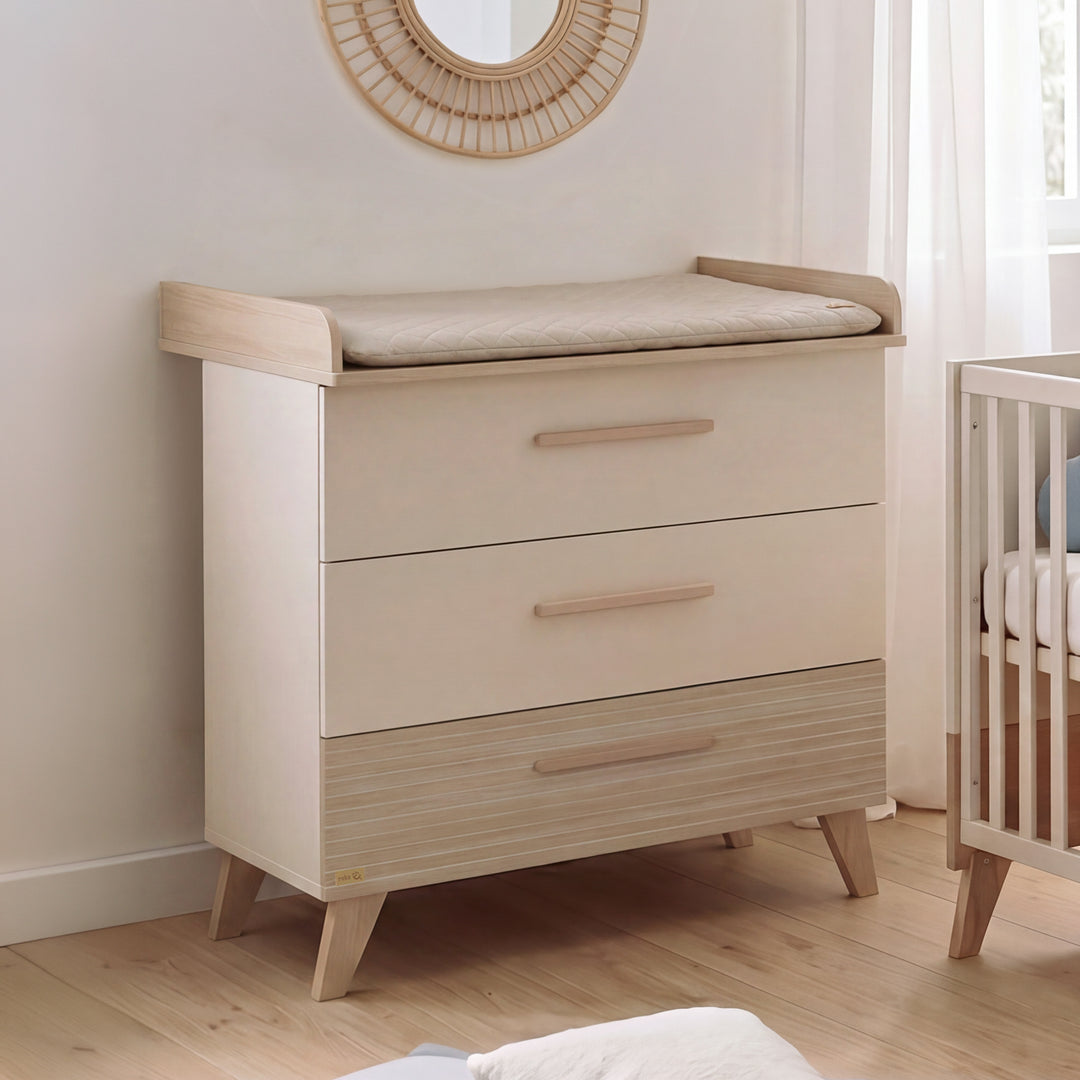 Wickelkommode 'Sidney' im Babyzimmer mit Wickelauflage, Rattan-Spiegel und Babybett im Hintergrund
