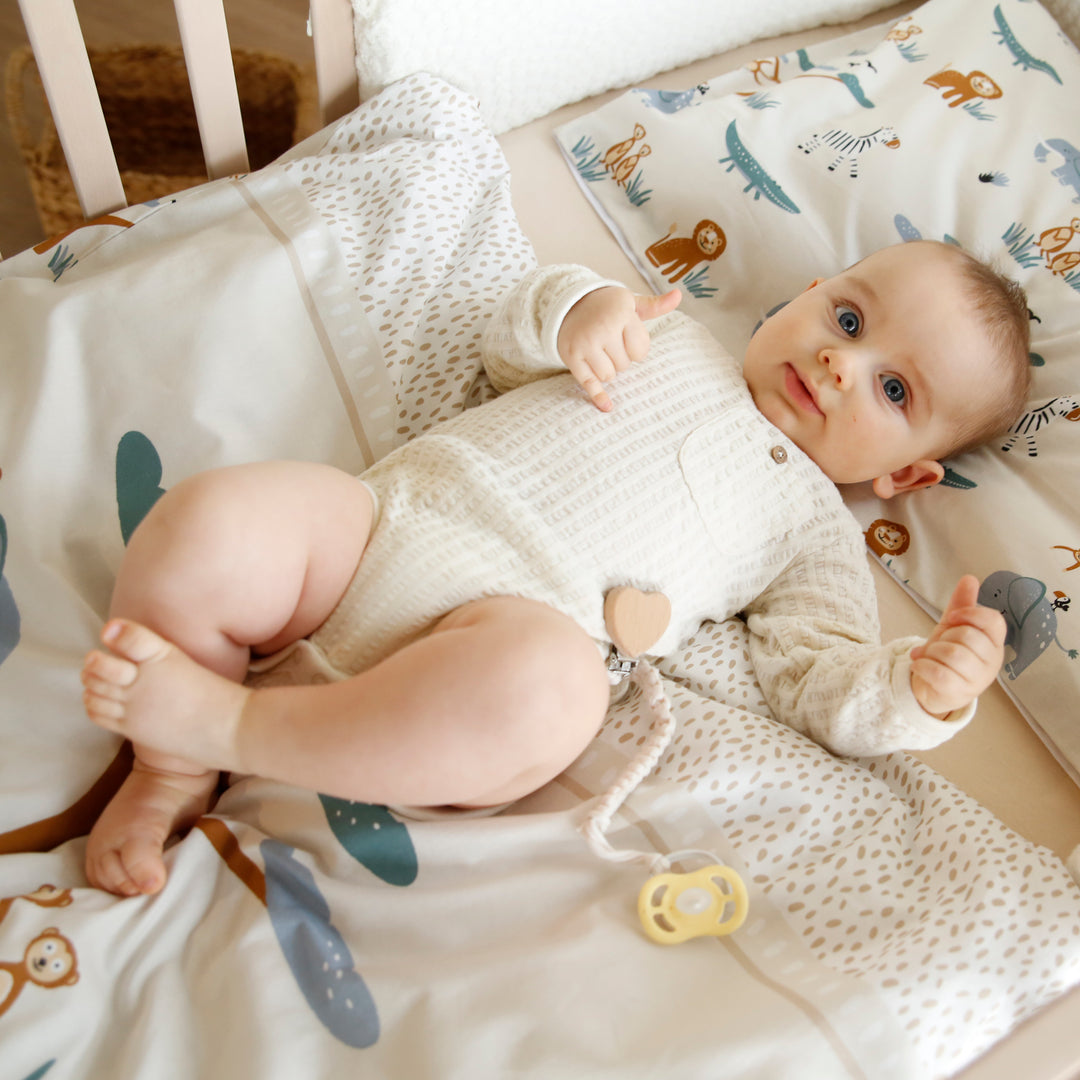 Bébé allongé dans le berceau sur le linge de lit "Savanna Friends" au motif animalier beige et bleu