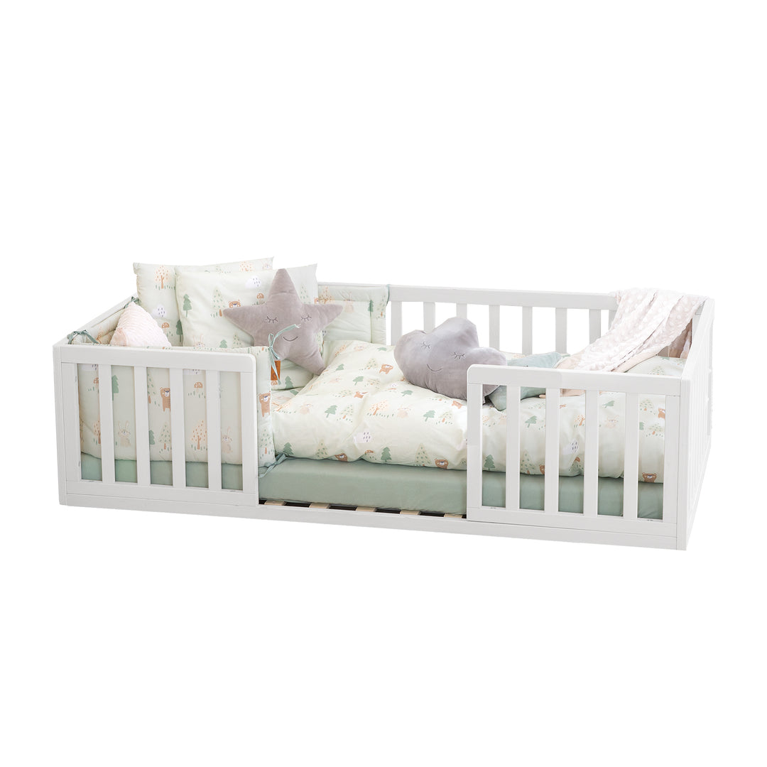 Lit bas laqué blanc, en bois, avec barrière de protection, linge de lit à motif forêt et coussins étoile et nuage, sur fond blanc