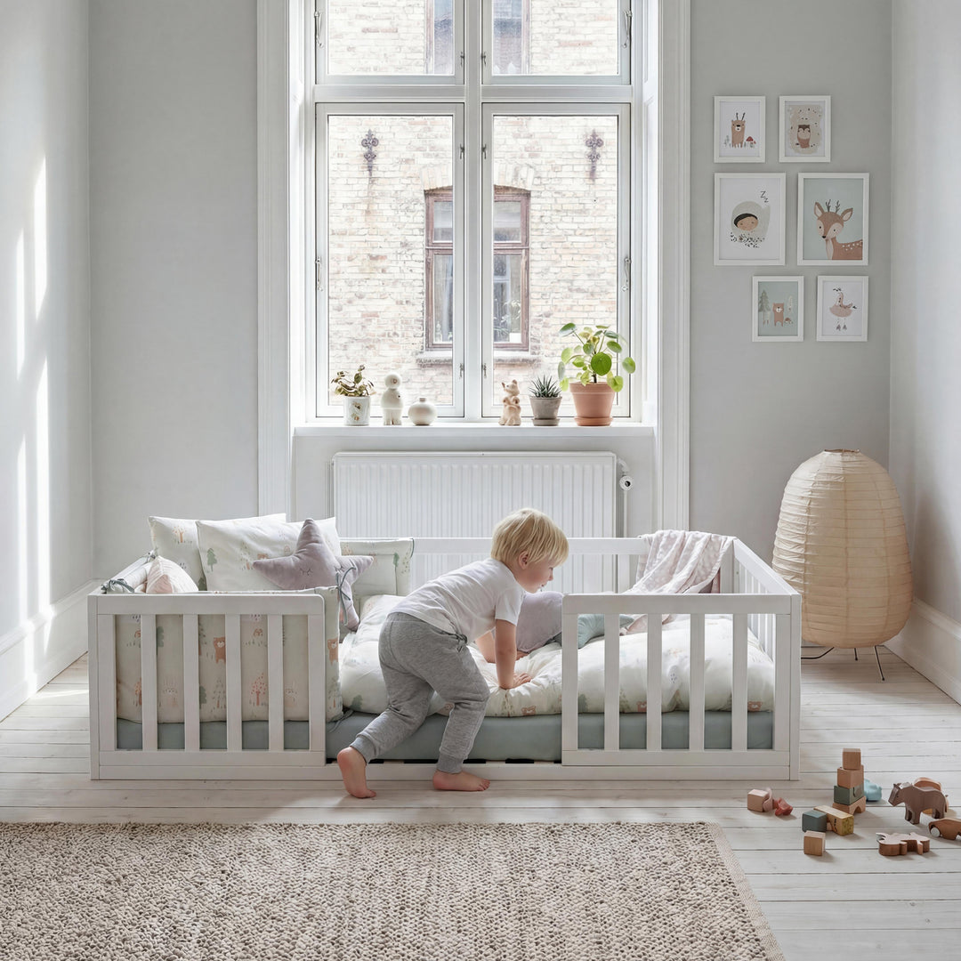 Lit bas Montessori laqué blanc, sur lequel un jeune enfant grimpe, dans une pièce lumineuse. Partiellement généré par IA