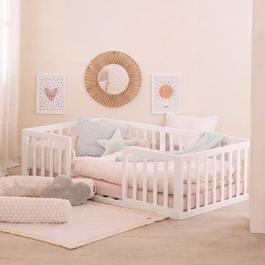 Lit bas Montessori laqué blanc dans une chambre d'enfant beige avec miroir en rotin, coussin en forme d'étoile et linge de lit rose