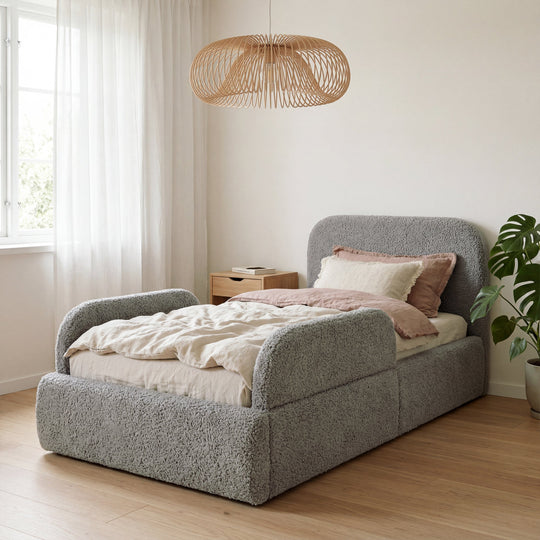 Cama infantil gris de bouclé con protección anticaídas en una habitación luminosa con lámpara de ratán y planta. Generada íntegramente con IA.