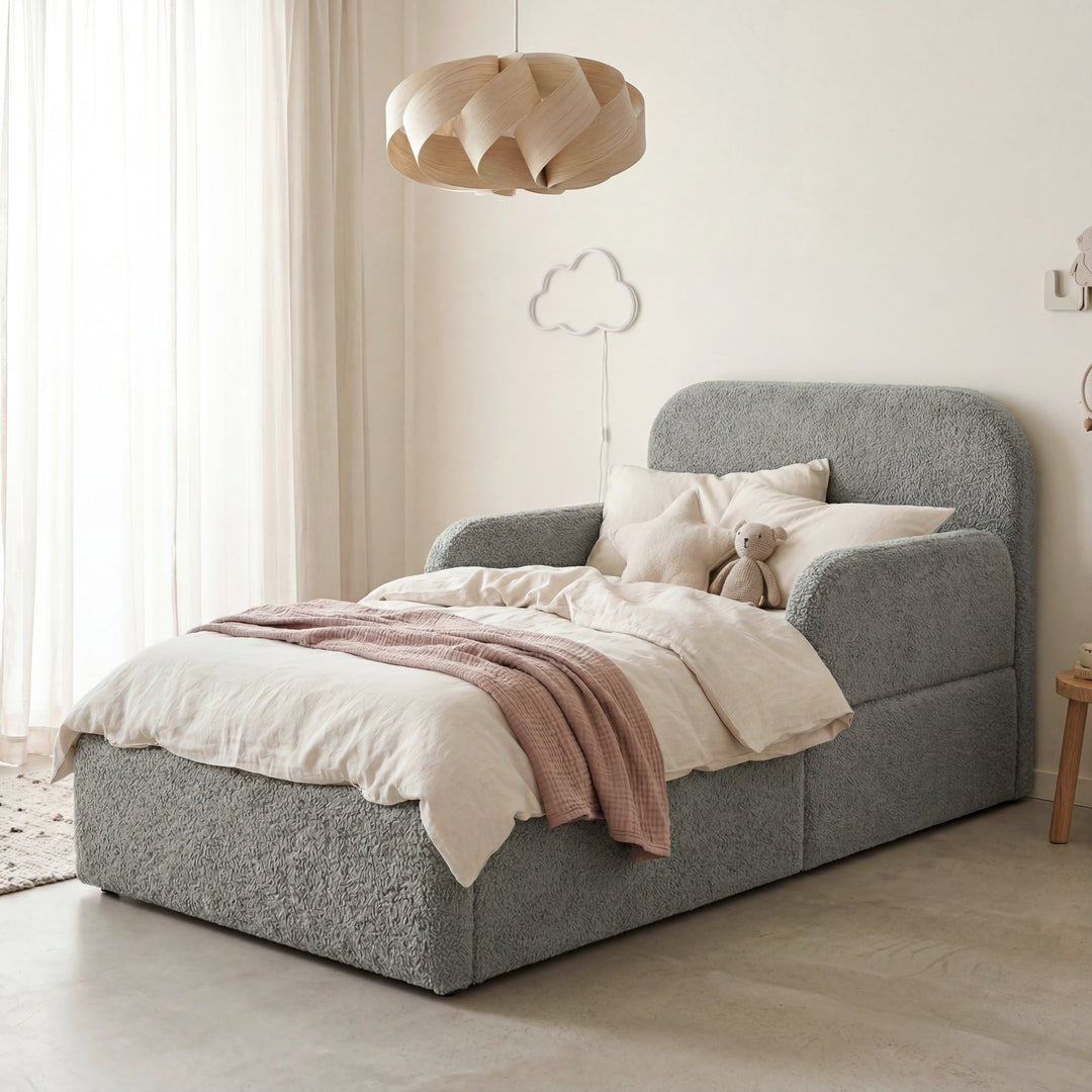 Cama infantil gris de bouclé con protección anticaídas, cojín, peluche y lámpara de nube en una habitación infantil. Generada íntegramente con IA.