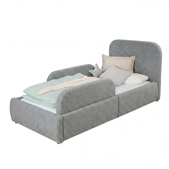 Cama infantil gris de bouclé con protección anticaídas y ropa de cama color menta, imagen recortada.