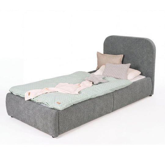 Cama infantil gris de bouclé con protección anticaídas vista desde los pies, ropa de cama color menta, imagen recortada.