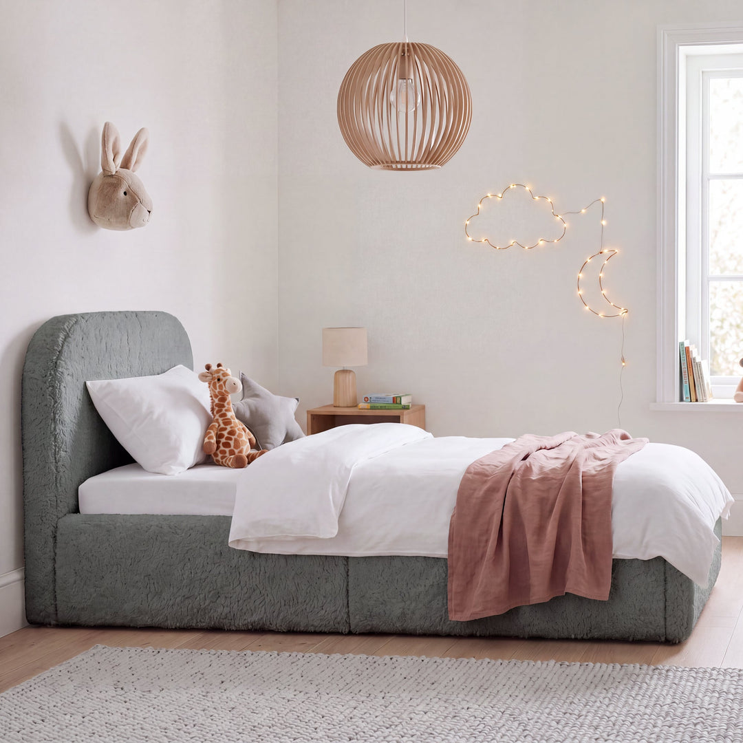 Cama infantil gris de bouclé con protección anticaídas, peluches y lámpara de madera en una habitación infantil. Generada íntegramente con IA.