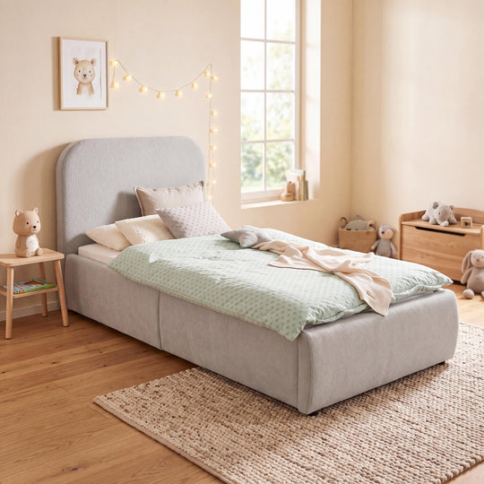 Cama infantil gris claro de bouclé con guirnalda de luces, cuadro y baúl de juguetes en una habitación infantil. Generada íntegramente con IA.