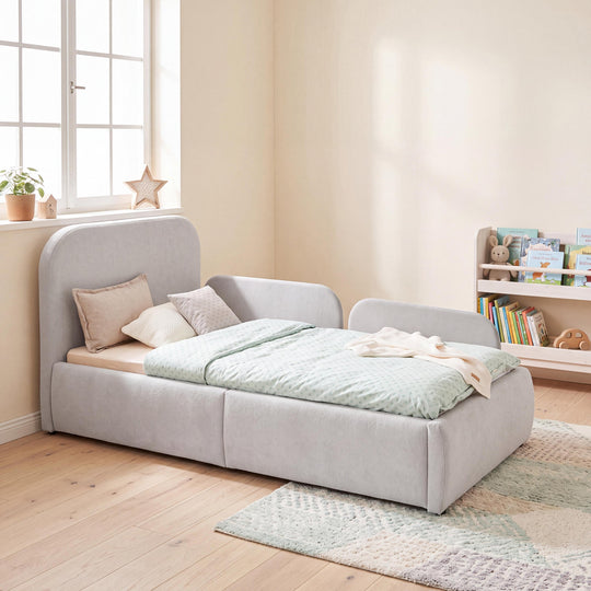 Cama infantil gris claro de bouclé con protección anticaídas y estantería de libros en una habitación infantil. Generada íntegramente con IA.