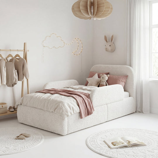 Cama infantil blanca de bouclé con protección anticaídas en una habitación luminosa con burro para ropa y guirnalda de luces. Generada íntegramente con IA.