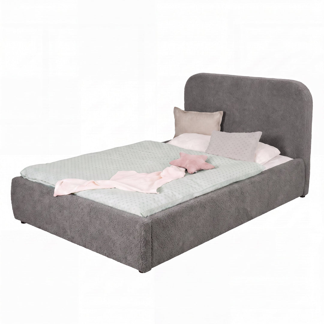 Cama gris de bouclé con ropa de cama rosa, recortada sobre fondo blanco.