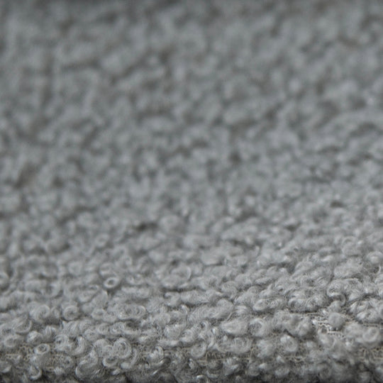 Close-up of the grey, textured bouclé fabric cover of the bed.
