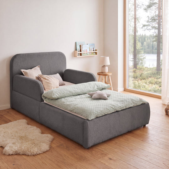Grey bouclé bed with bedside lamp, bookshelf and forest view in the room. Fully AI-generated.