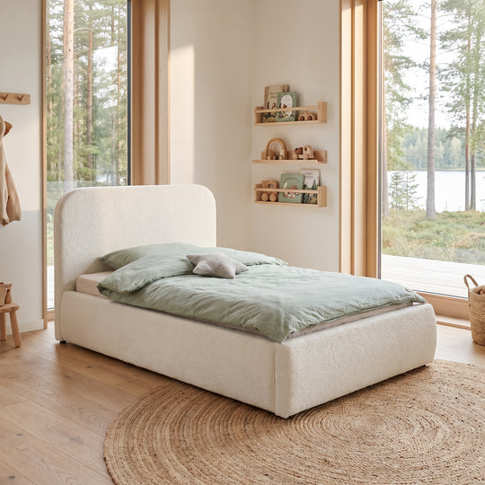 White bouclé bed in front of a large window front with bookshelf and forest view. Fully AI-generated.