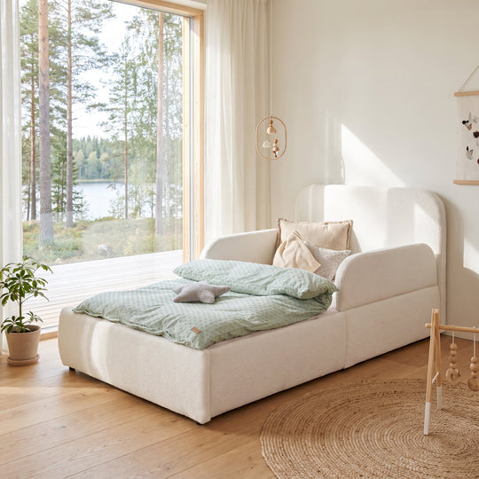 White bouclé bed with hanging mobile, plant and forest view in the room. Fully AI-generated.