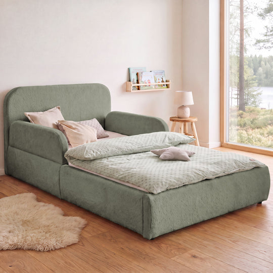 Sage green roba Little Dream children's bed in a children's room with lake view, bookshelf and sheepskin rug. Partially AI-generated.