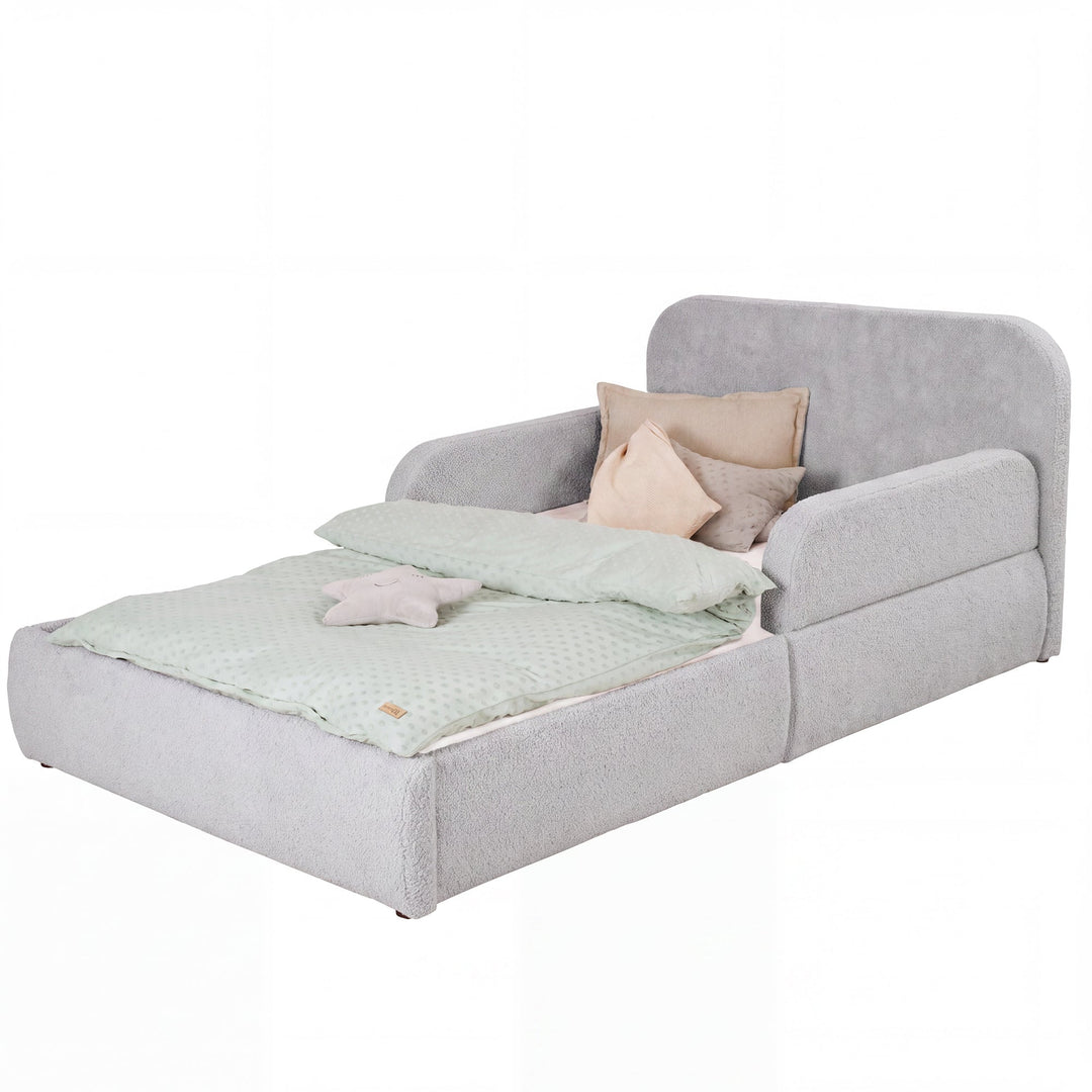 Cama infantil roba Little Dream gris claro con cabecero y protecciones laterales, vestida con ropa de cama y cojines. Generada parcialmente con IA.